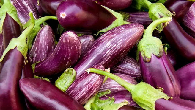 A pile of fresh eggplants, some solid dark purple and others striped purple and white, with green stems.